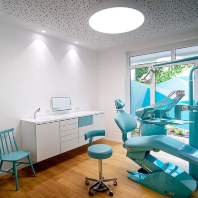 Behandlungsraum bei MKG Plus in Münster mit türkisem Behandlungsstuhl und weiteren türkisen Stühlen, sowie einem Holzbodenbelag.