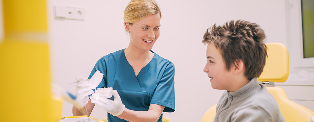 Eine Zahnärztin zeigt einem Jungen das Gipsmodell seiner Zähne.