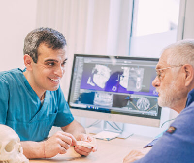 Zahnarzt Dr. Kedir zeigt einem Patienten die Funktionsweise von Keramikimplantaten.