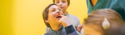 Headerbild in dem ein Junge freudig eine Zahnlücke mit einem nachwachsenden Zahn vorzeigt.
