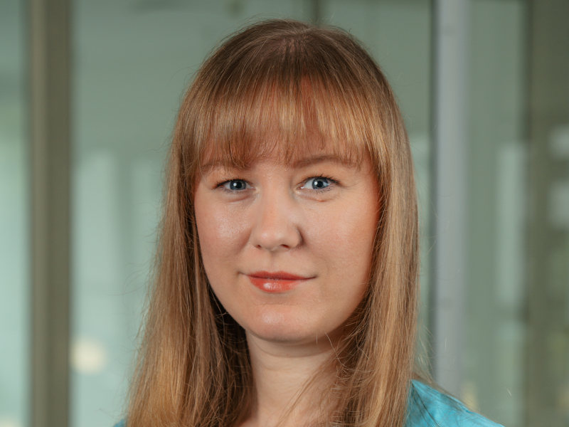 Das Bild zeigt Iuliia Kulcicki, eine Zahnmedizinische Fachangestellte. Sie trägt hellblaue medizinische Kleidung und lächelt freundlich in die Kamera. Iuliia Kulcicki hat lange, glatte, blonde Haare mit einem Pony.