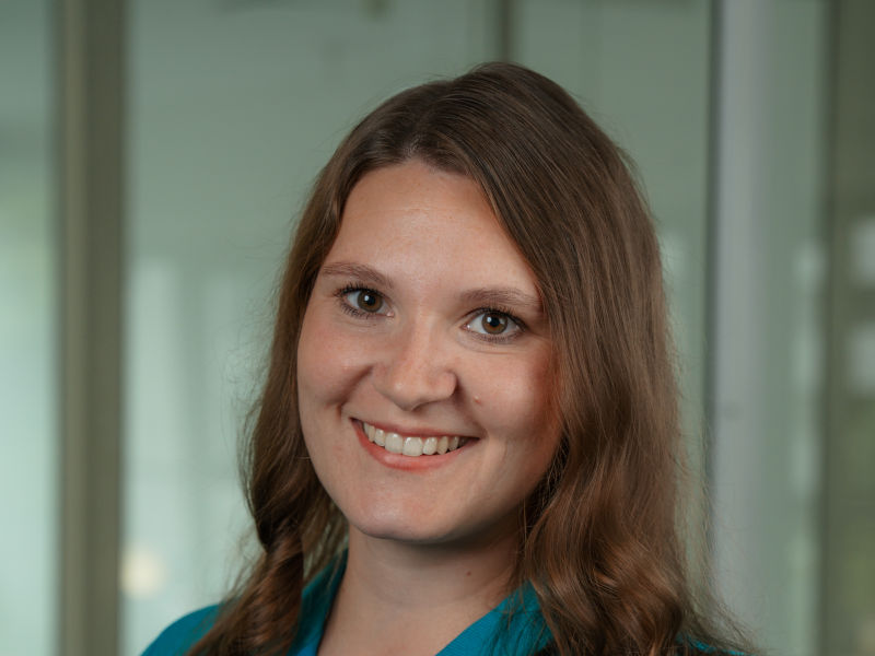 Das Bild zeigt Sarah Wyczisk, Zahntechnikerin bei Zahnärzte MKG+ Münster. Sie trägt blaue, medizinische Arbeitskleidung und lächelt freundlich in die Kamera.