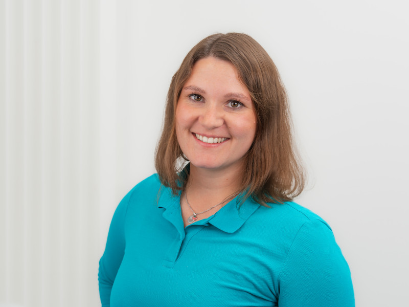 Das Bild zeigt Sarah Wyczisk, Zahntechnikerin bei Zahnärzte MKG+ Münster. Sie trägt ein blaues Poloshirt und lächelt freundlich in die Kamera.