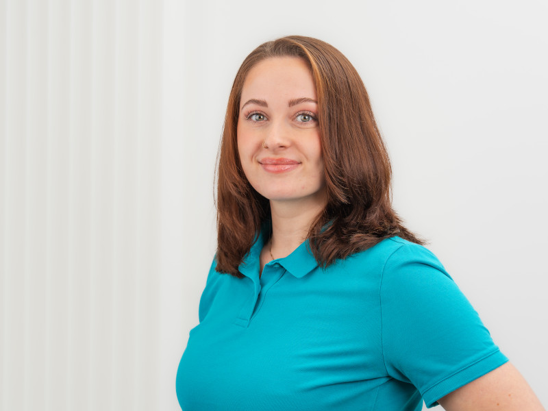 Das Bild zeigt Vanessa Wagenknecht, Zahntechnikerin ZFA bei Zahnärzte MKG+ Münster. Sie trägt ein blaues Poloshirt, und lächelt freundlich in die Kamera.
