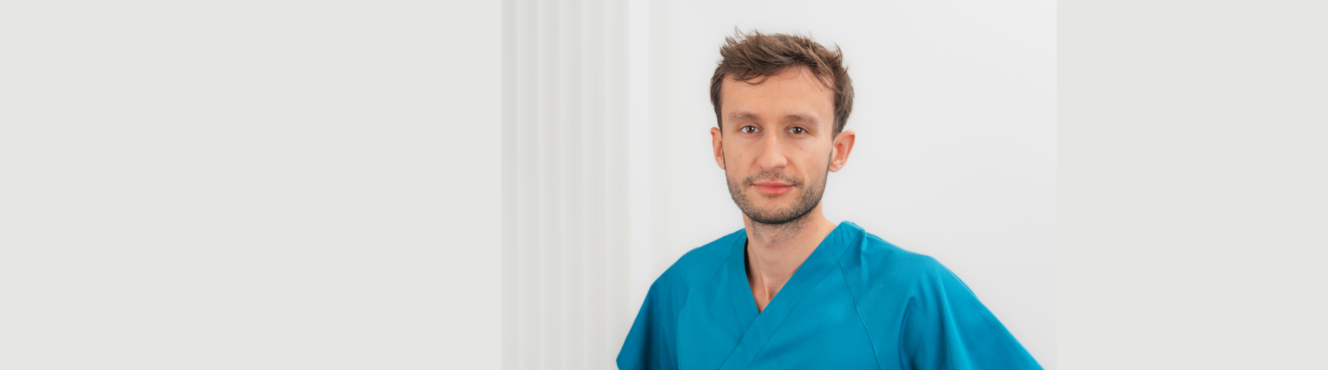 Das Bild zeigt Klemens Utzel, einen Zahnarzt in Münster. Er hat kurze, braune Haare und lächelt freundlich in die Kamera. Klemens Utzel trägt eine blaue medizinische Kleidung. Der Hintergrund ist hell und schlicht gehalten.