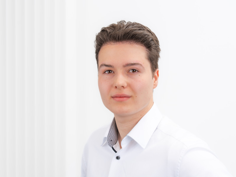 Porträt von Jan Luca Grüneberg-Nolte, Mitarbeiter im Bereich Empfang und Verwaltung der Zahnklinik MKG Plus in Münster. Er trägt ein helles Hemd und blickt in die Kamera. Sein dunkelblondes Haar ist ordentlich frisiert.